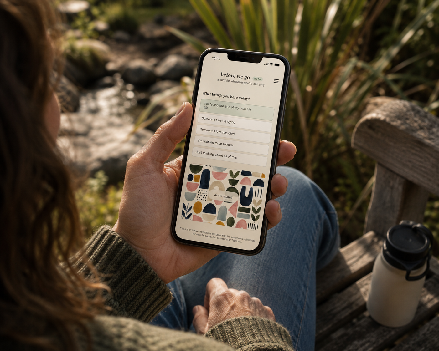 A person sitting outdoors holding a phone showing the Before We Go reflection cards